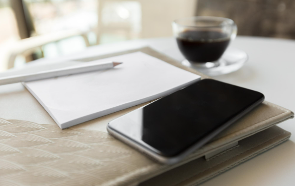 From Paper Slips to Phone Screens in Fifty Years – Golf News Coffee cup beside notebook, pen, and smartphone on table.